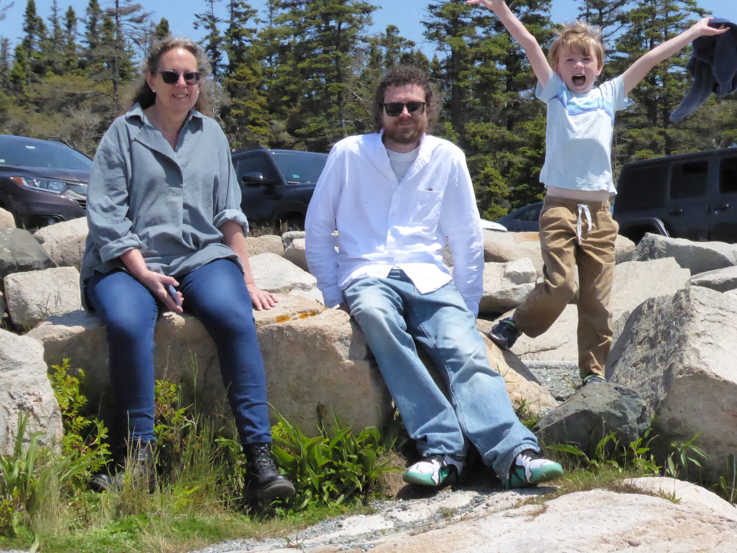 Woman (Margaret) and younger man (Nate) in sunglasses, sitting on boulder